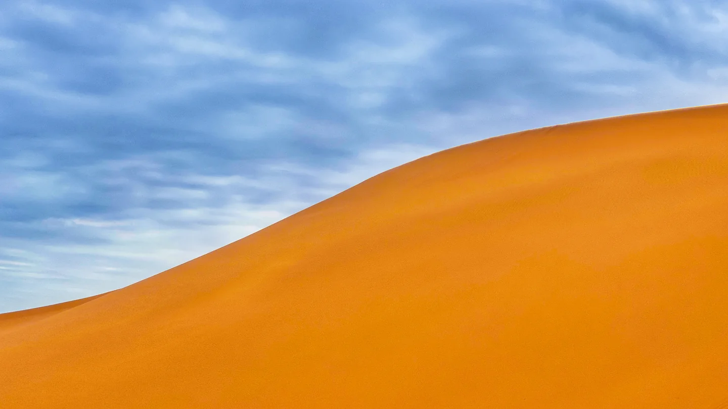A golden sand dune rises beneath rippled blue-gray clouds.