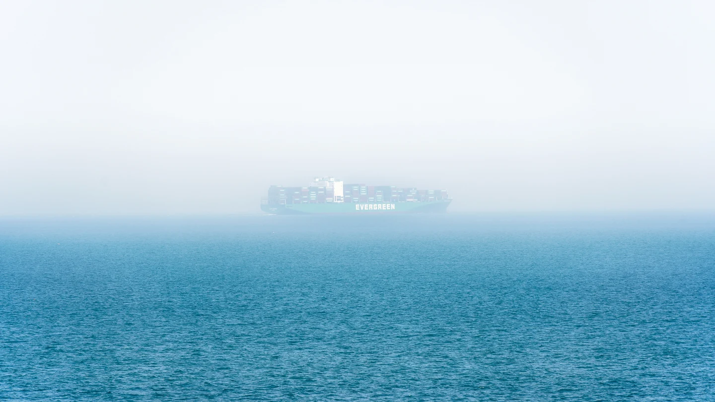 A solitary cargo ship appears through pale mist above a blue sea.
