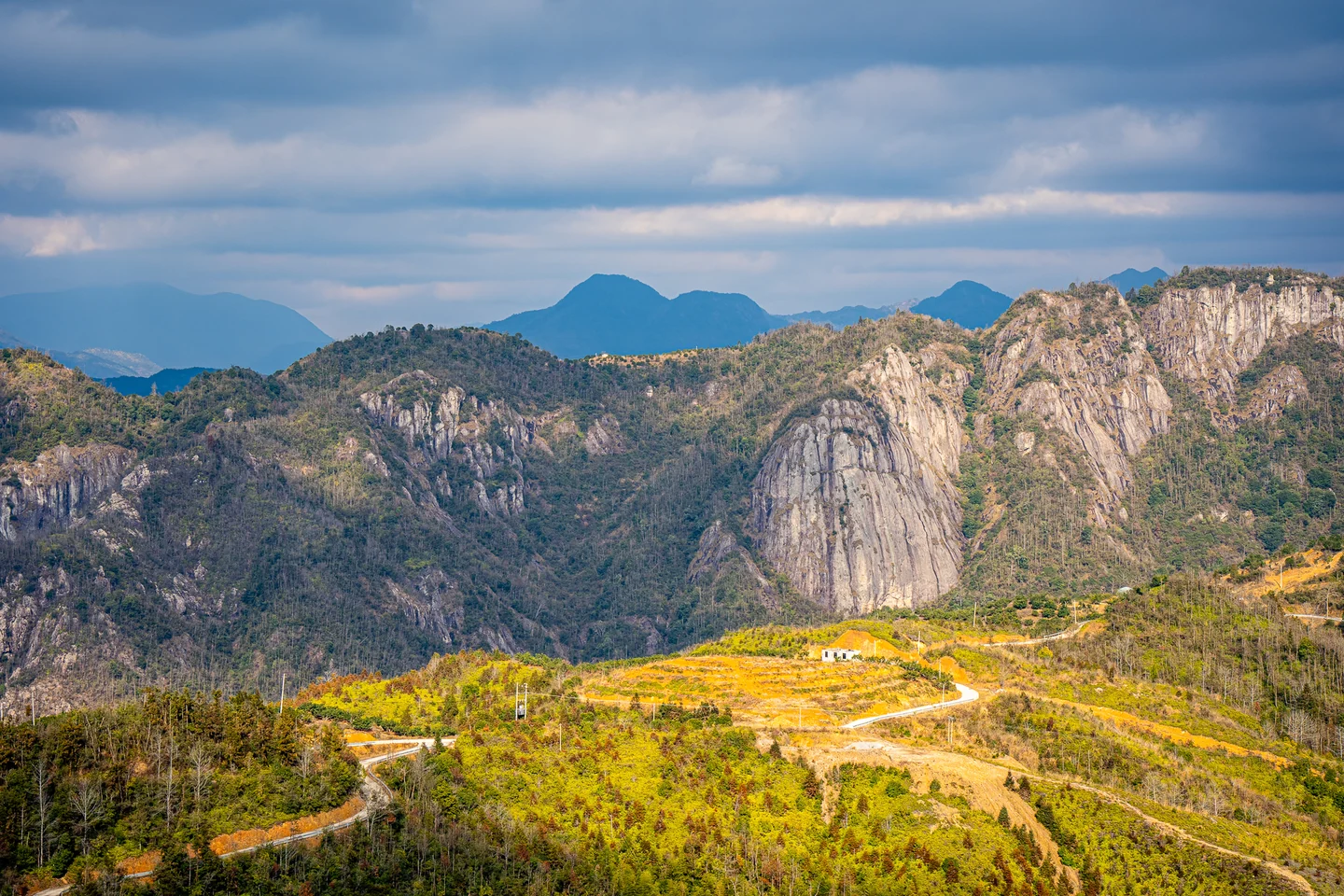 Golden and green fields spread beneath a dramatic rocky mountain wall.