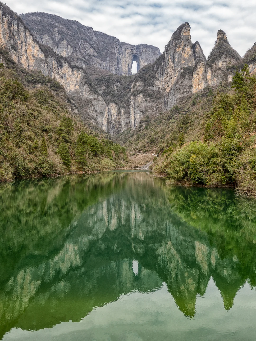 Sharp mountain peaks and green slopes are reflected in a still green lake.