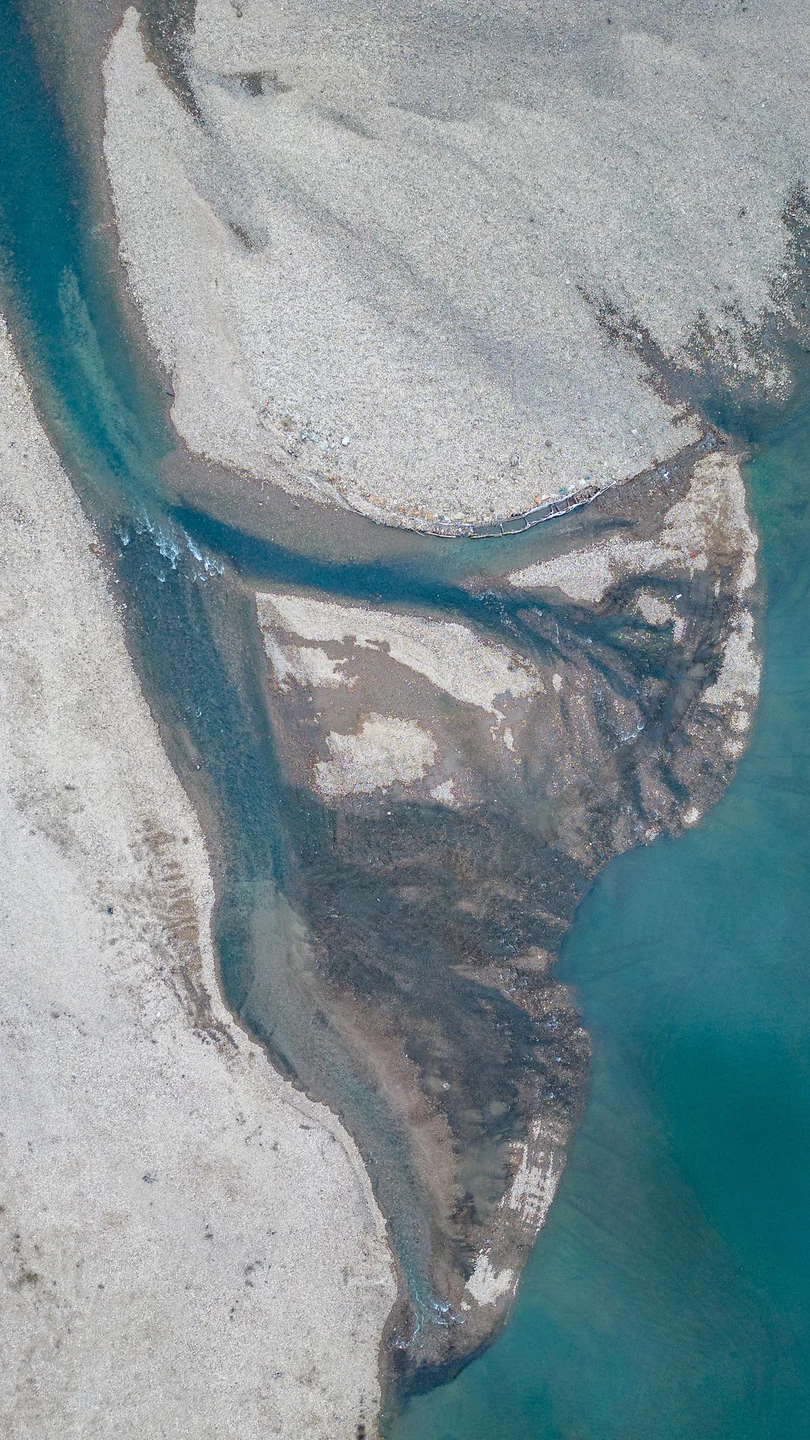 A turquoise channel curves between pale tidal flats, seen from above.
