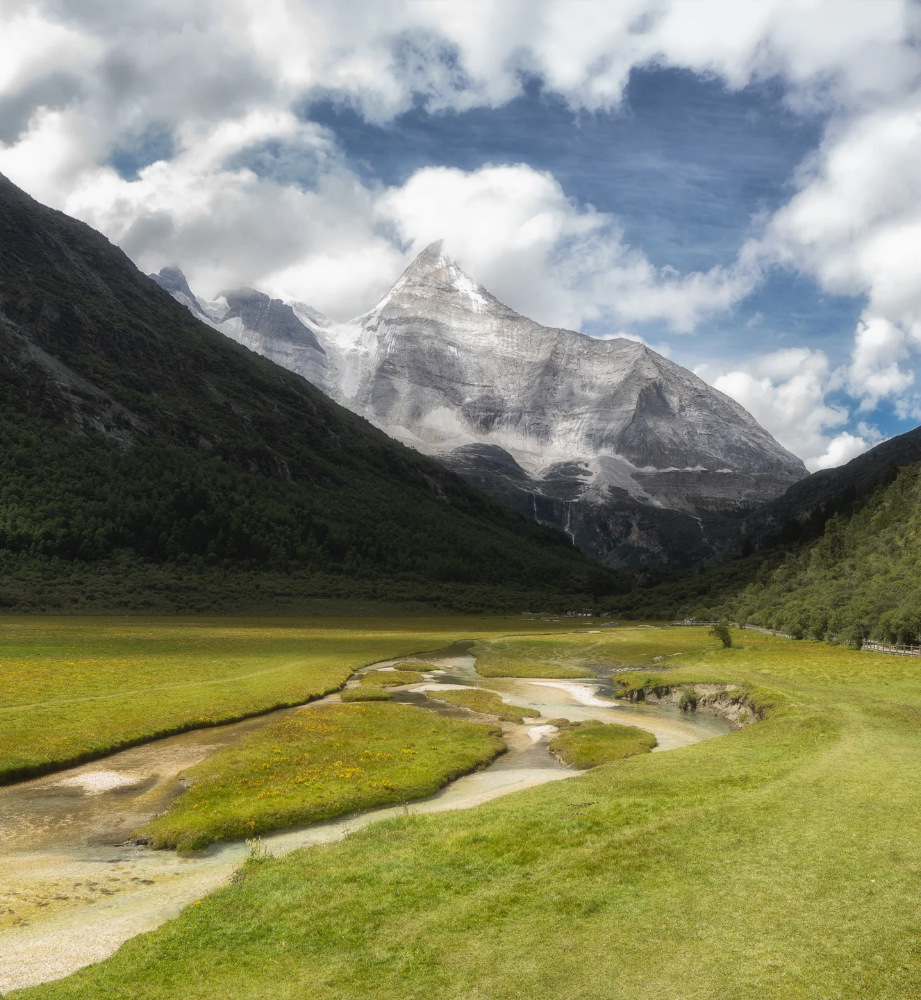 A winding stream crosses a green valley toward a snow-covered mountain.