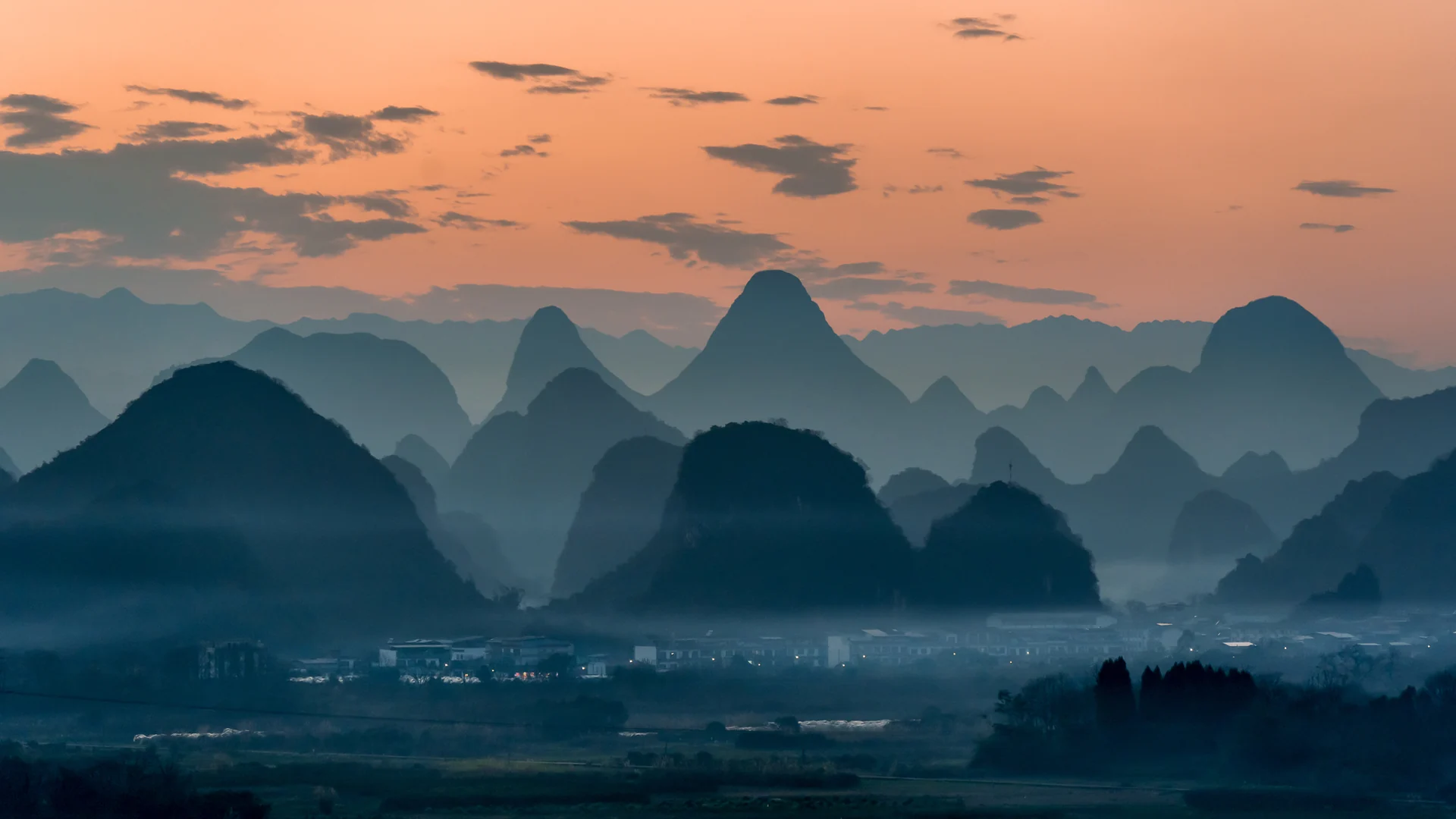 Layers of karst peaks fade into blue haze beneath a peach-colored evening sky.